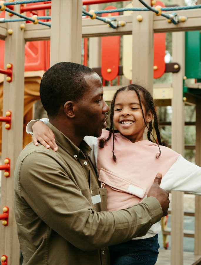 Young father holding smiling daughter on climbing frame